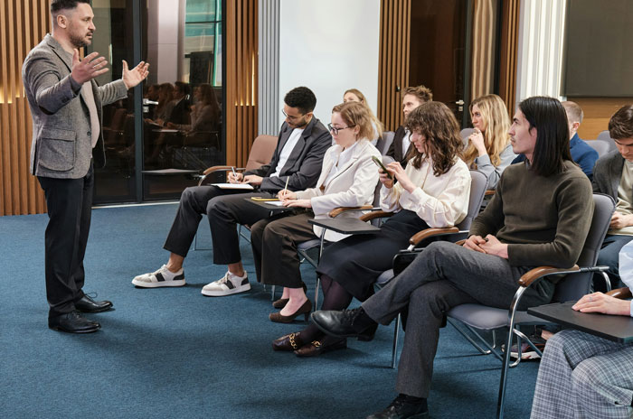Man presenting to a seated audience in a conference room discussing secrets spouses keep after marriage.