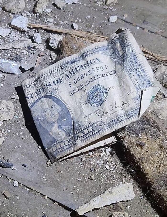 Worn one dollar bill lying on dusty floor surrounded by rubble in homes with hidden or haunted pasts.