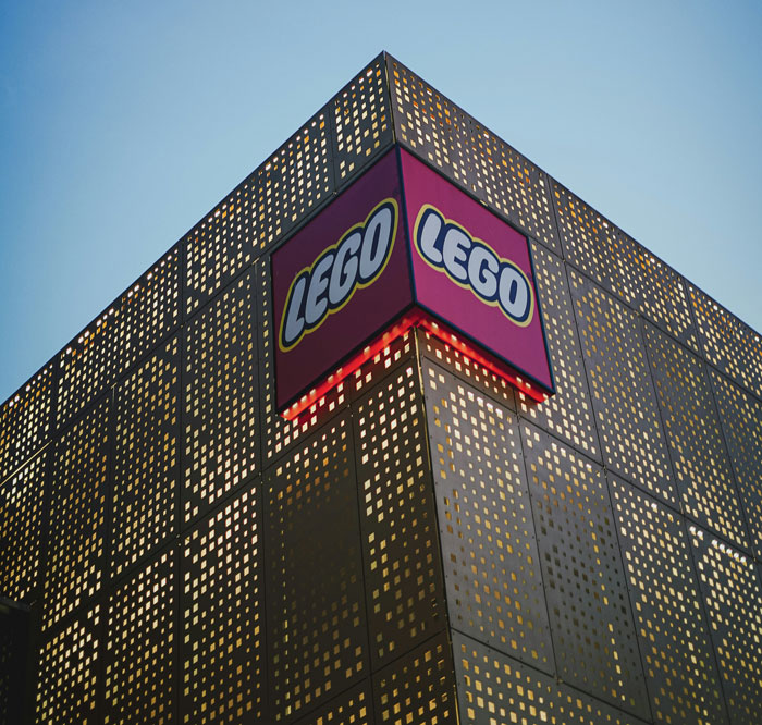 Exterior view of a modern building with a LEGO logo, symbolizing former employees revealing disturbing workplace secrets.