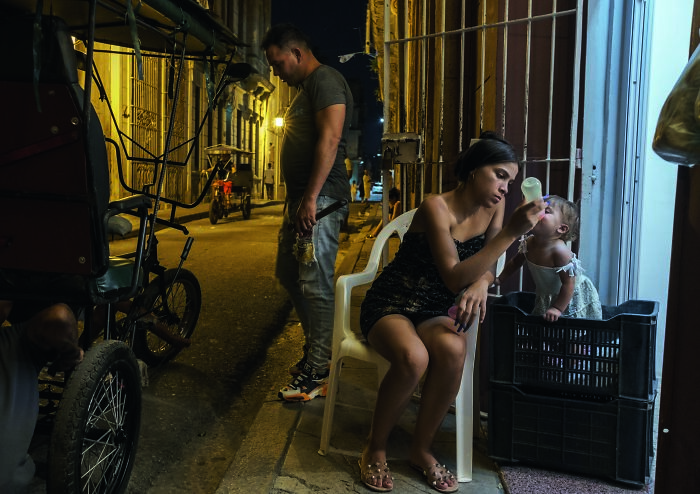 Young mother feeding baby at night in a dimly lit street, capturing the essence of humanity in IPA 2024 Best Of Show.