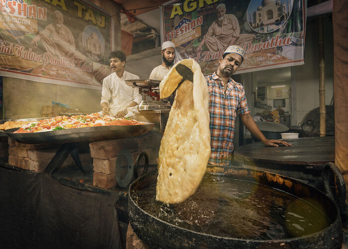 Man cooking traditional flatbread in large pan at a busy food stall, captured in breathtaking food photography.