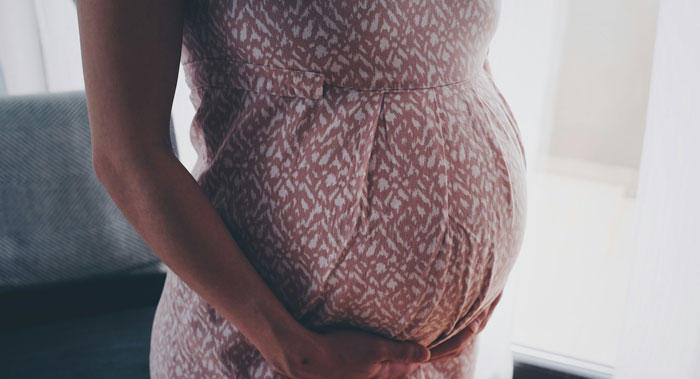 Pregnant woman cradling her belly indoors, representing teen son getting girlfriend pregnant on purpose concept.