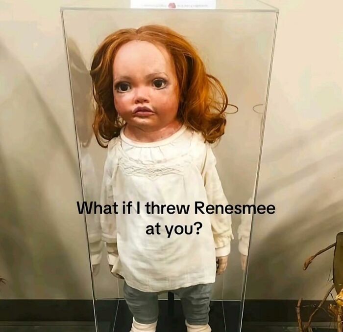 Creepy doll with red hair and white outfit behind glass case in a cute and wholesome posts collection.