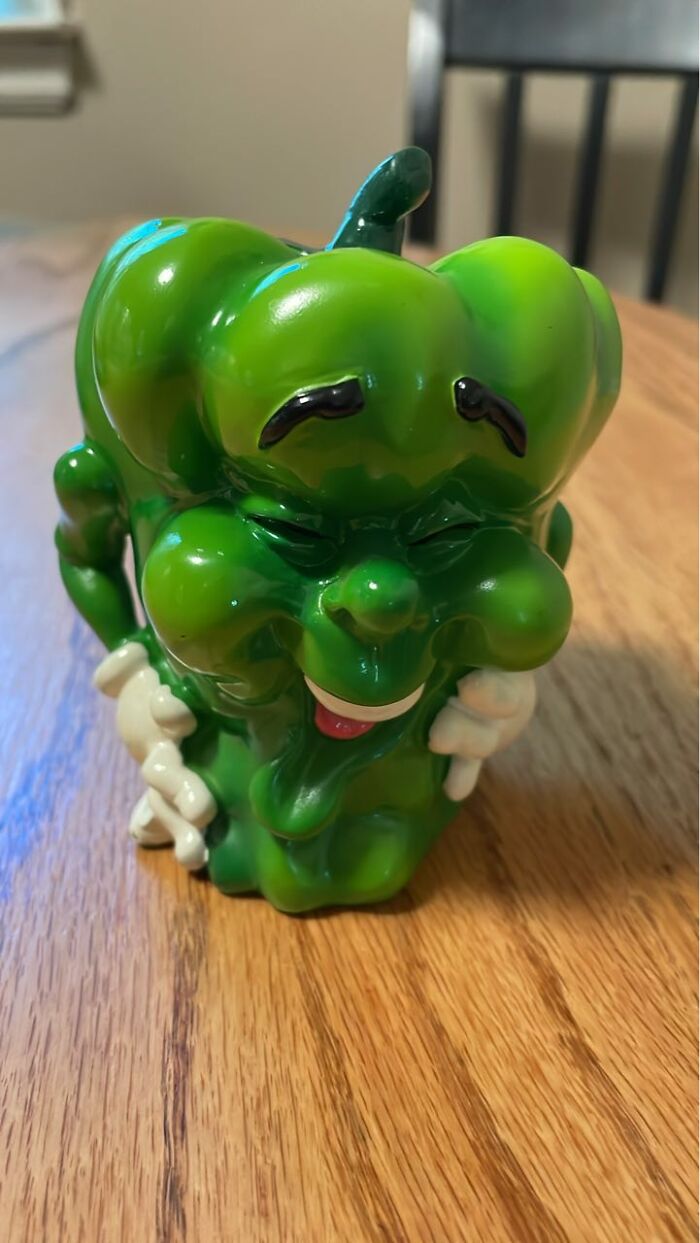 Green quirky ceramic figurine with a smiling face and whimsical expression on a wooden table, thrifted find.