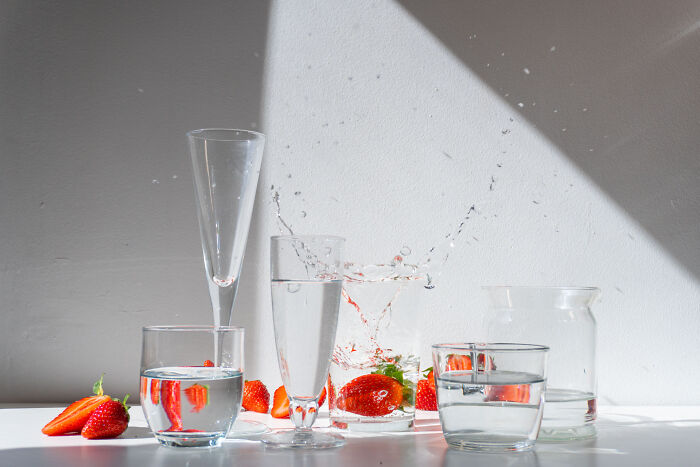 Glassware filled with water and fresh strawberries captured in a dynamic food photography shot with splash effects.