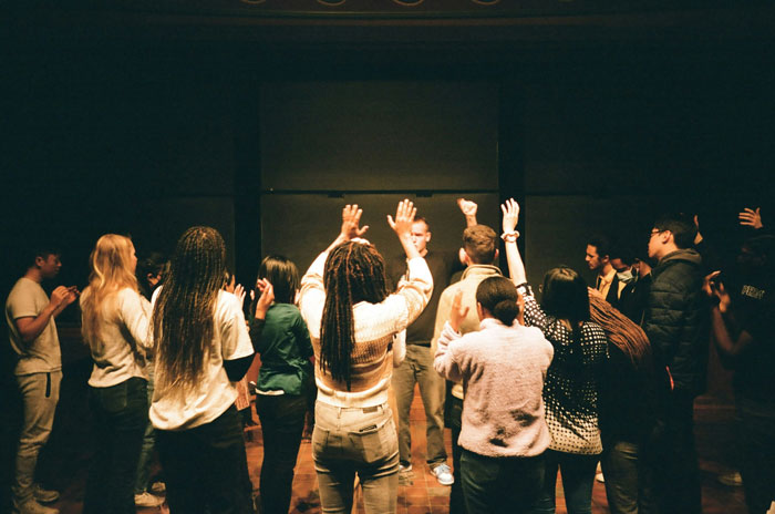 Group of people raising hands in a dim room, symbolizing experiences of people who escaped from cults and their stories.