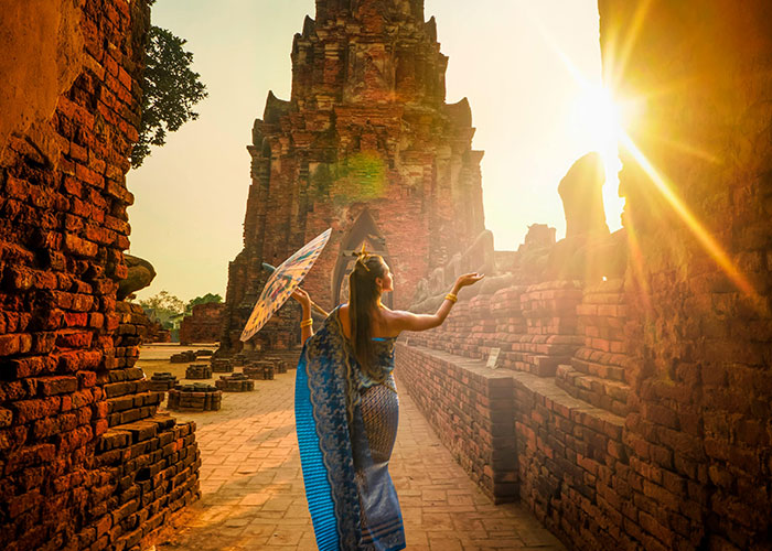 Woman in traditional dress with umbrella exploring ancient ruins at sunset, sharing best and worst things about living in home countries