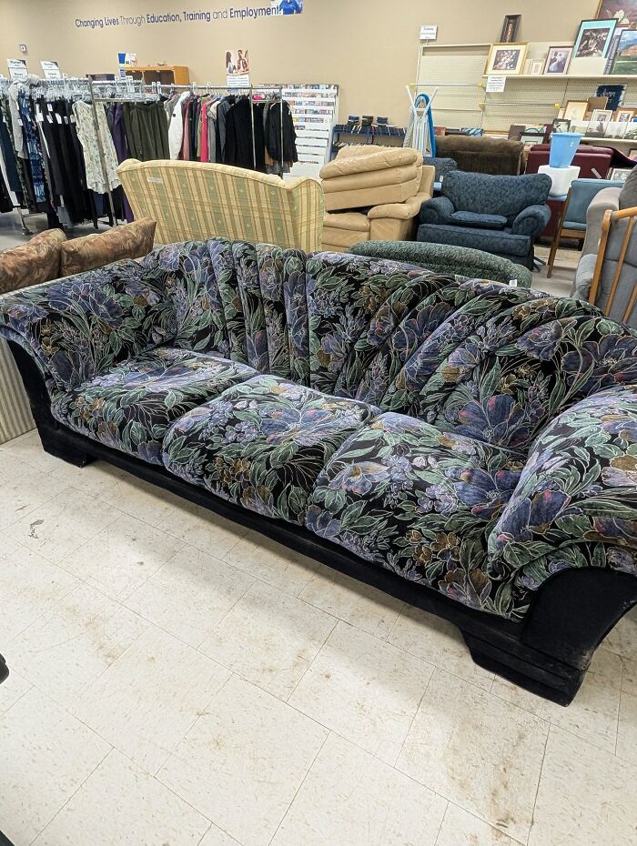 Floral patterned thrifted sofa with a curved back in a thrift store filled with eclectic vintage furniture.