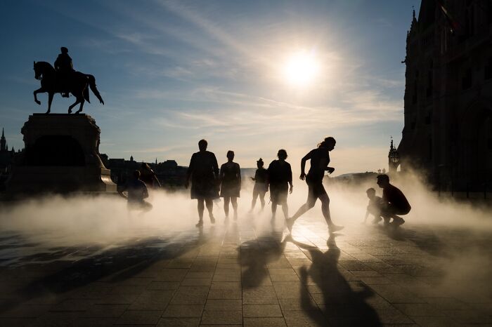 Silhouettes of people walking through mist in a city square, showcasing pure street photography in dynamic urban light.