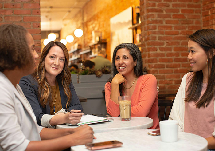 Four women having a candid conversation in a cozy cafe discussing problematic behaviors women get a pass for according to men.