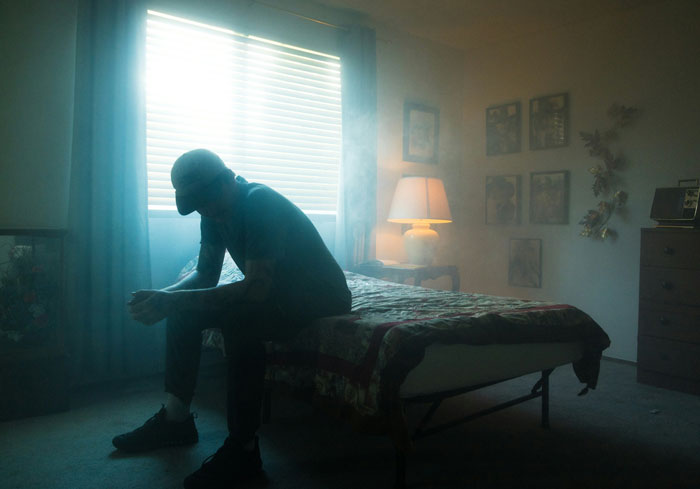 Silhouetted person sitting on a bed in a dimly lit room, reflecting on experiences escaping from cults.