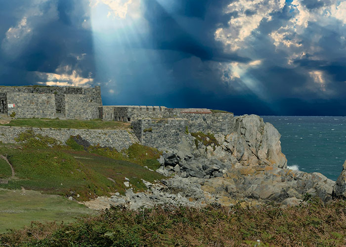 Stone fortress on rocky coastline under dramatic sky showing the best and worst things about living in home countries.