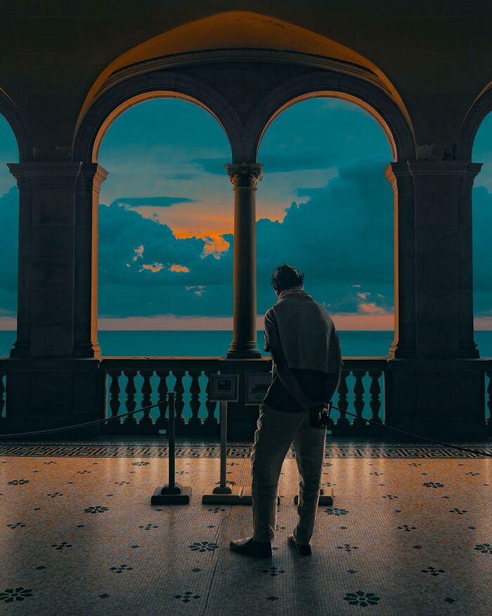 Person standing under arches looking at ocean at sunset in a surreal creative photo edit that questions reality.