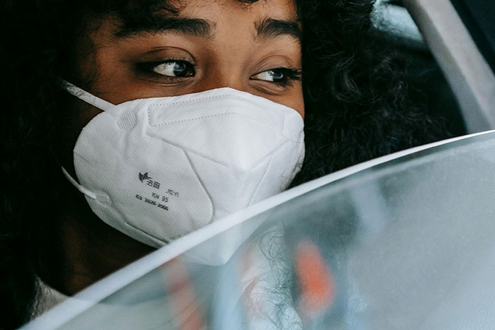 Person wearing a protective mask looking outside a car window with a worried expression, reflecting a gut feeling to leave.