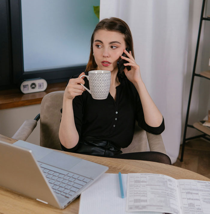 Young woman on phone at home office holding a mug, reflecting on friendship of 10+ years ended and reasons shared.