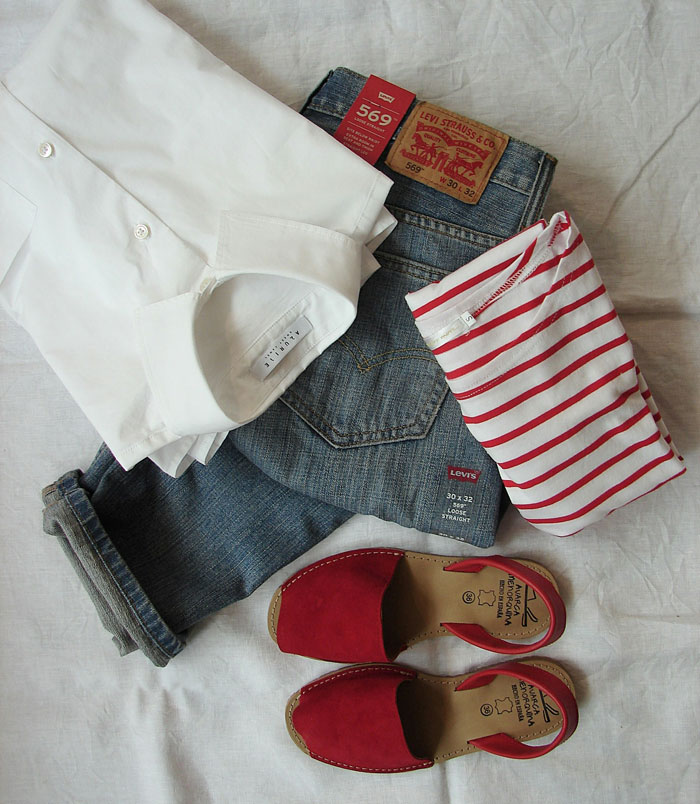 Folded white shirt, striped top, Levi's jeans, and red sandals laid out on a white fabric background, showing everyday clothing habits.