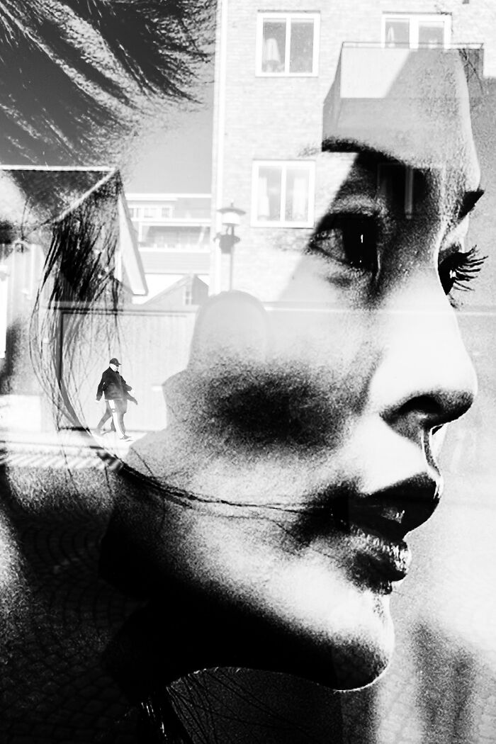 Abstract black and white street photography showing a profile of a woman's face with a walking figure and buildings reflected.