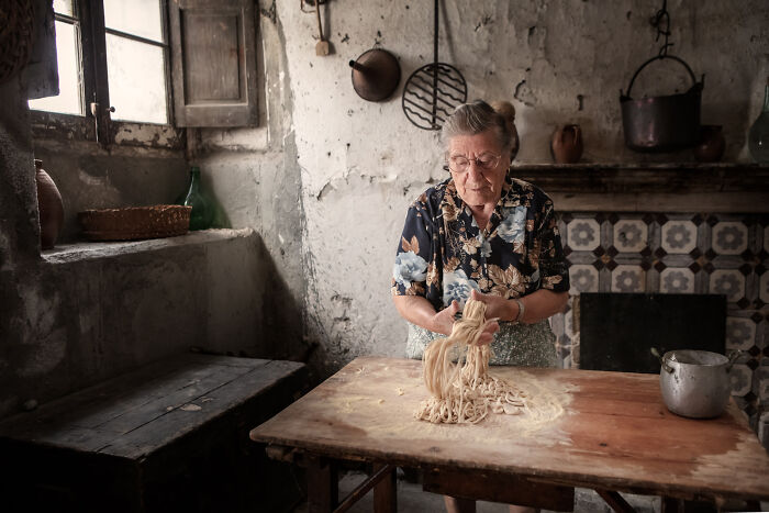 Elderly woman preparing fresh pasta in rustic kitchen captured in breathtaking food photography award-winning style.