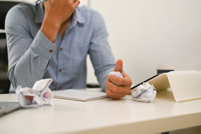 Person stressed at desk with crumpled paper, reflecting on experiences related to escaping cults and sharing stories.