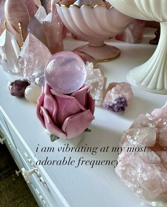 Pink crystals and a rose-shaped holder with a clear sphere, surrounded by various healing stones on a white surface.