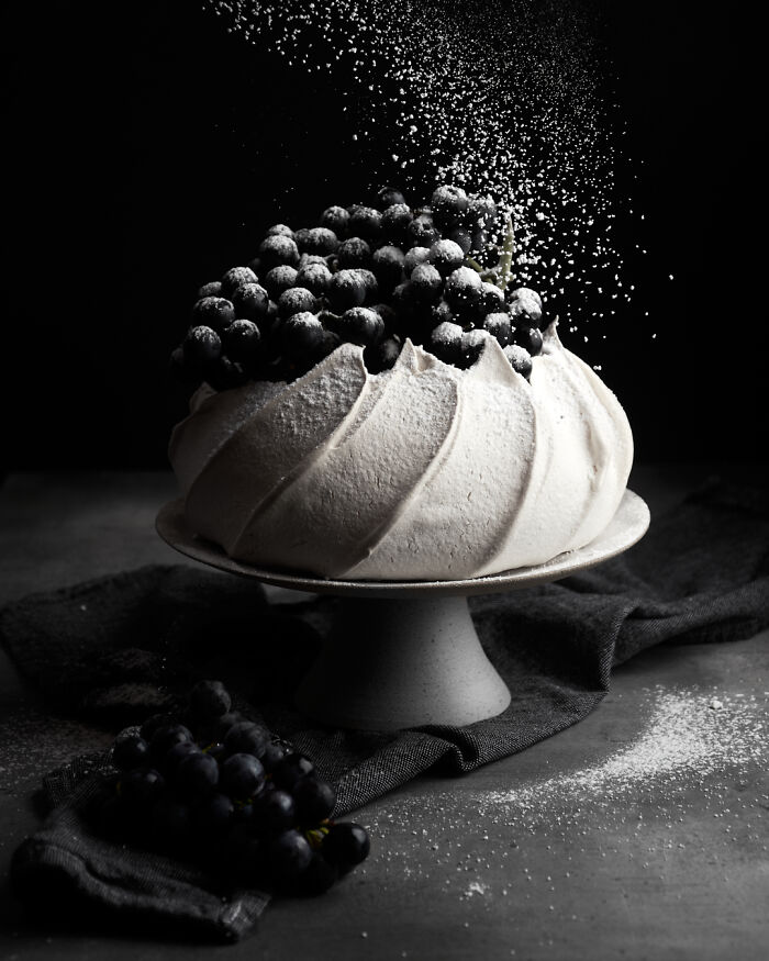 A dessert topped with grapes has powdered sugar sprinkled over it, showcasing world food photography awards quality.
