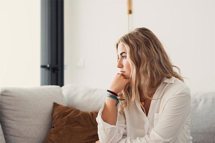 Young woman sitting thoughtfully on a couch, reflecting on demanding to check brother’s girlfriend’s bags before leaving. Young woman sitting thoughtfully on a couch, reflecting on demanding to check brother’s girlfriend’s bags before leaving.