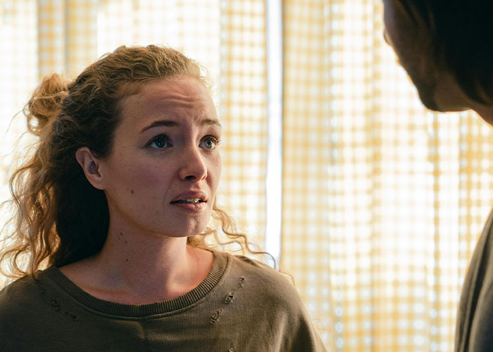 Woman with troubled expression discussing emotional trauma with boyfriend in a softly lit room after newborn incident.