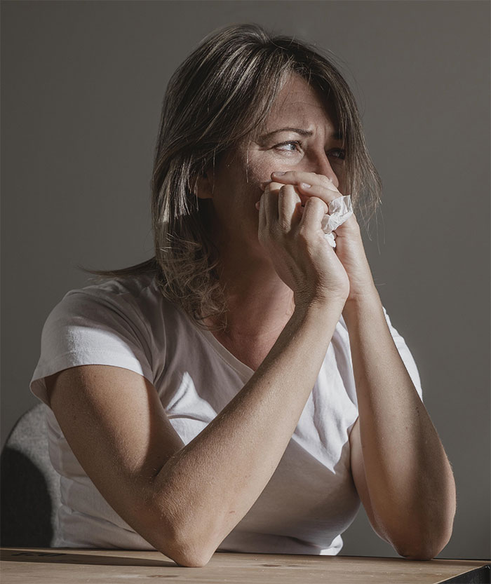 Woman with cancer looking distressed while sitting at a table, holding a tissue and reflecting on chores and support.