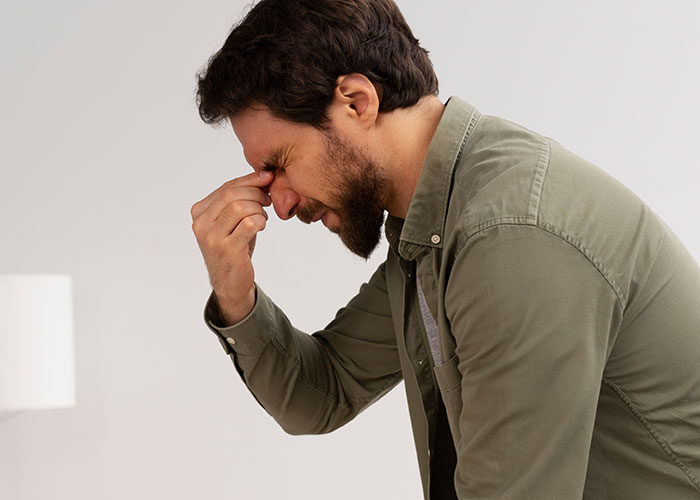 Man in casual shirt showing stress or frustration, representing employee standing up to boss in office conflict scenario.