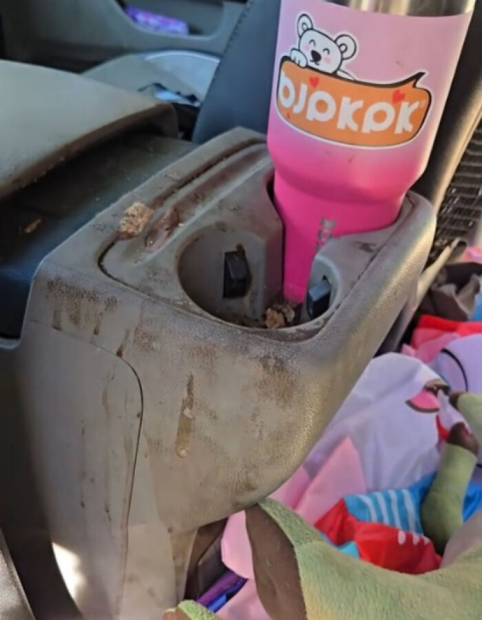 Dirty car cup holder with crumbs and a pink bottle, highlighting the challenge of cleaning out a filthy car interior.