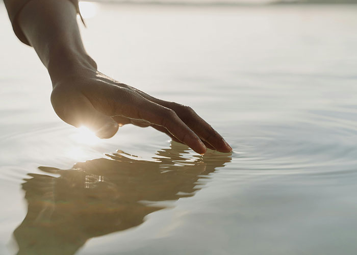 A hand gently touching calm water reflecting sunlight, illustrating surprisingly entertaining facts shared in a thread.