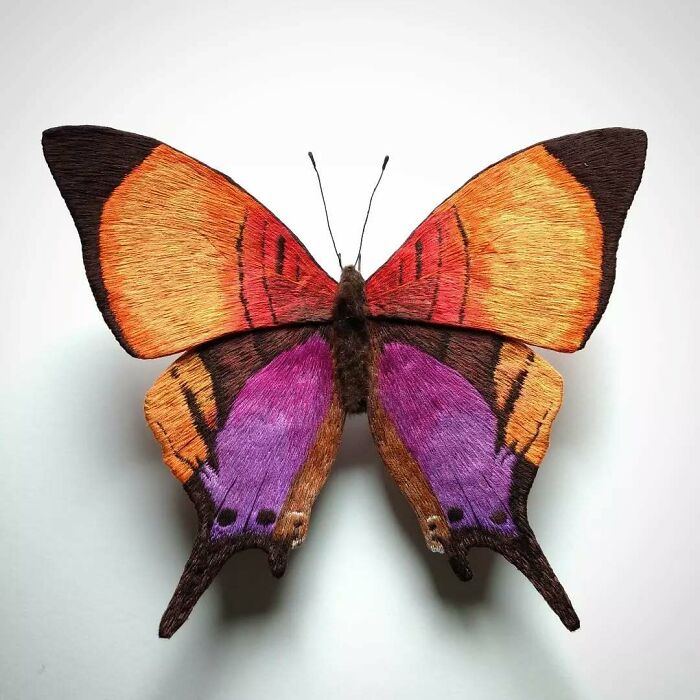 Embroidered fiber butterfly with vibrant orange, red, and purple wings showcasing detailed textile art by Yumi Okita.