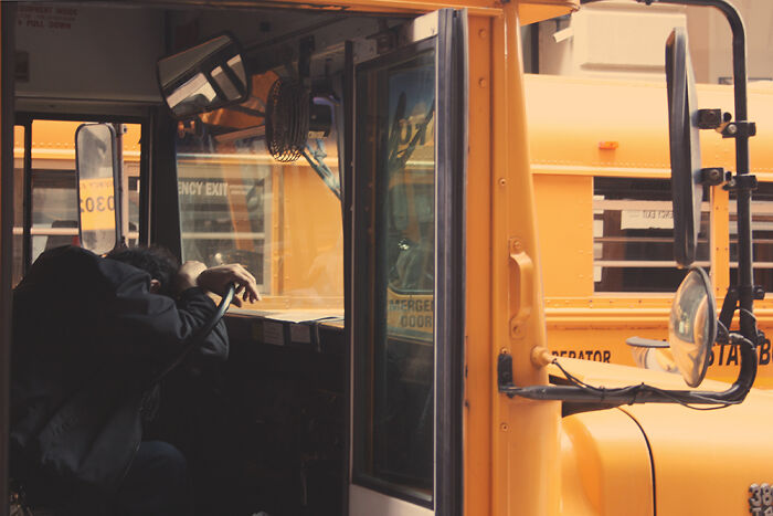 A person resting inside a school bus captured in a candid street photography moment by talented photographers.