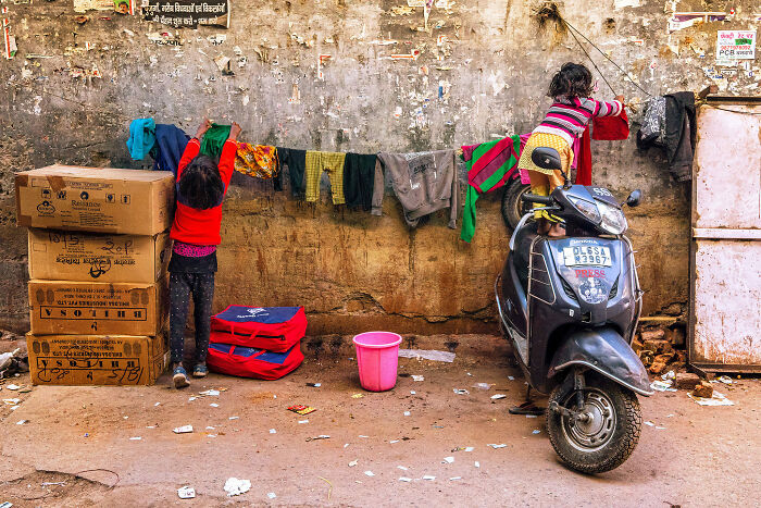 Two children hanging colorful clothes on a line in a street photography moment captured by talented photographers.