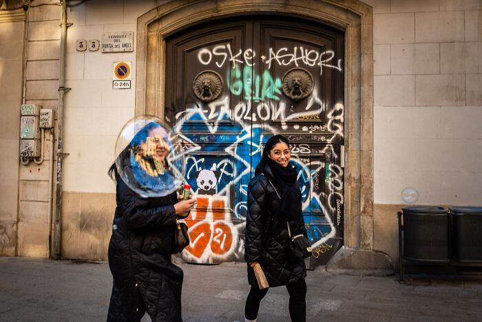 Two women walking past a graffiti-covered door, capturing vibrant street photography moments in an urban setting.