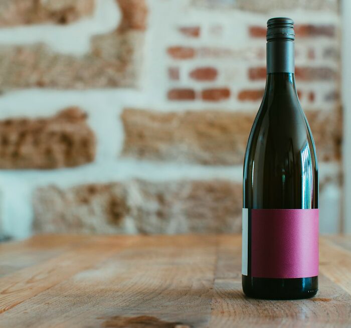 Wine bottle with a blank maroon label on a wooden table against a rustic brick wall background.