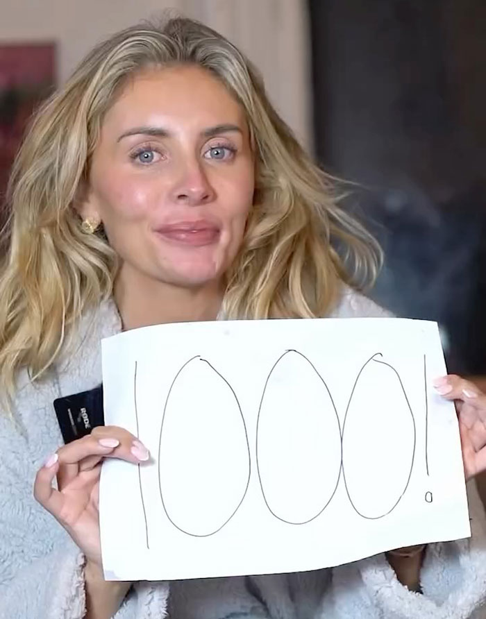 Blonde woman holding a sign with 1000 written, related to Bonnie Blue posts and adult star arrest update.