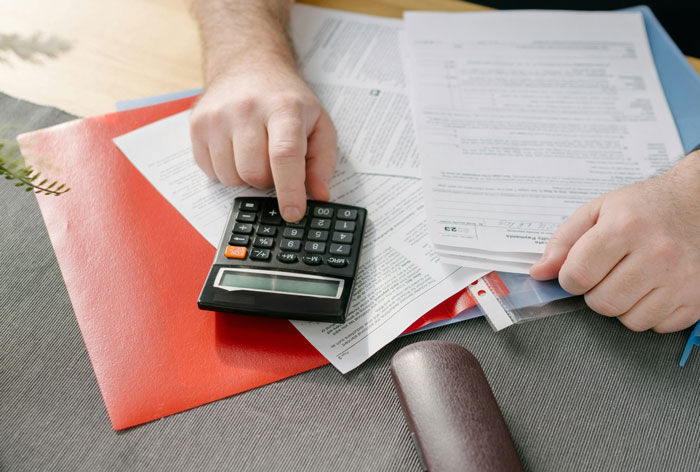 Person using a calculator and reviewing financial documents, illustrating common ways people lose money while saving.
