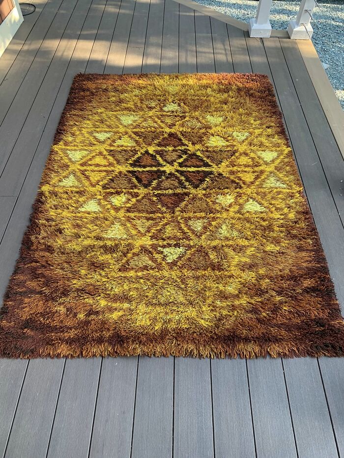 Vintage thrifted s**g rug with geometric patterns in warm brown and yellow tones on outdoor deck.