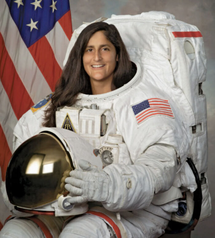 Astronaut in a space suit holding helmet, representing astronauts who spent 286 days in space and their post-mission struggles.