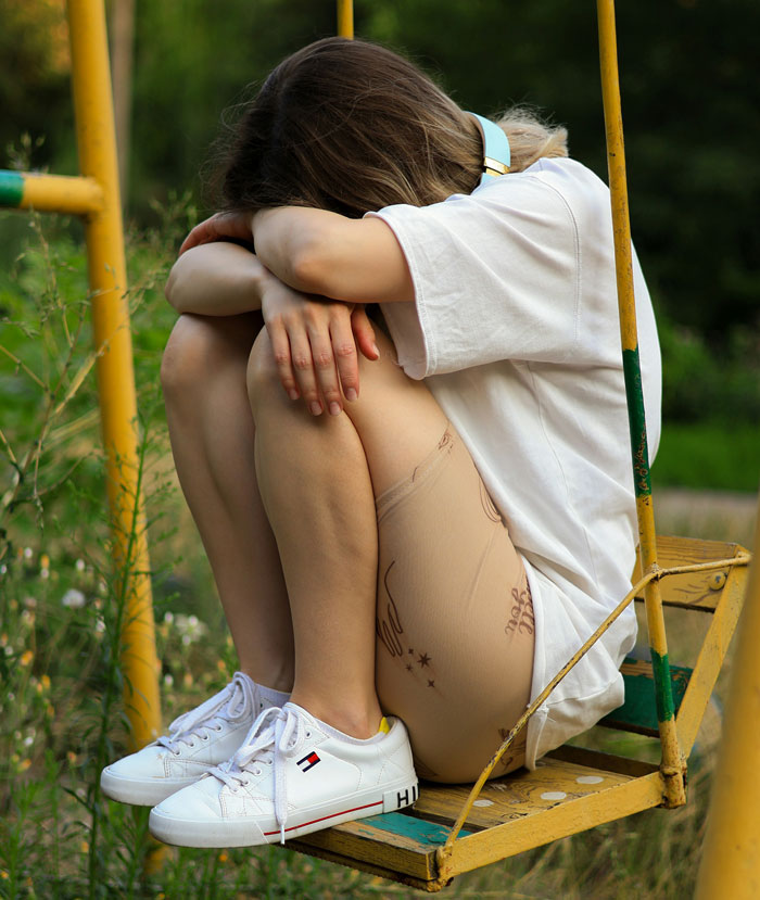 Young person sitting curled on a yellow swing, showing emotions of distress in a natural outdoor setting related to people who escaped cults.