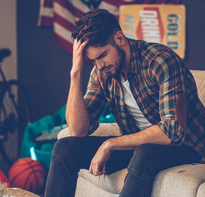 Young man sitting on a couch, looking down and stressed, reflecting on losing a good friend after years of friendship