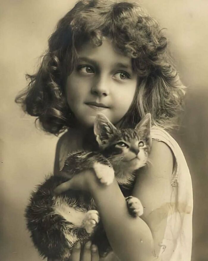 Vintage photo of a young girl holding a cat, highlighting the timeless bond between kids and cats.