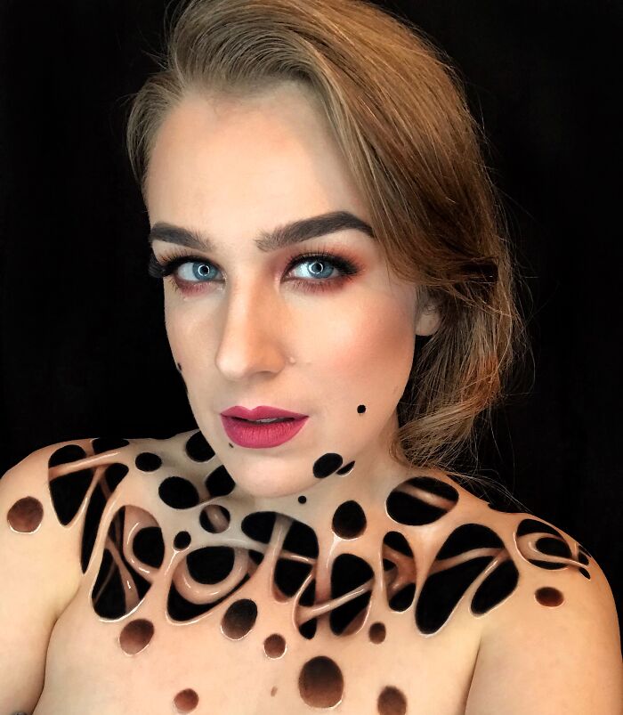 Woman with creative makeup looks and body paint featuring black abstract patterns on her shoulders and chest.