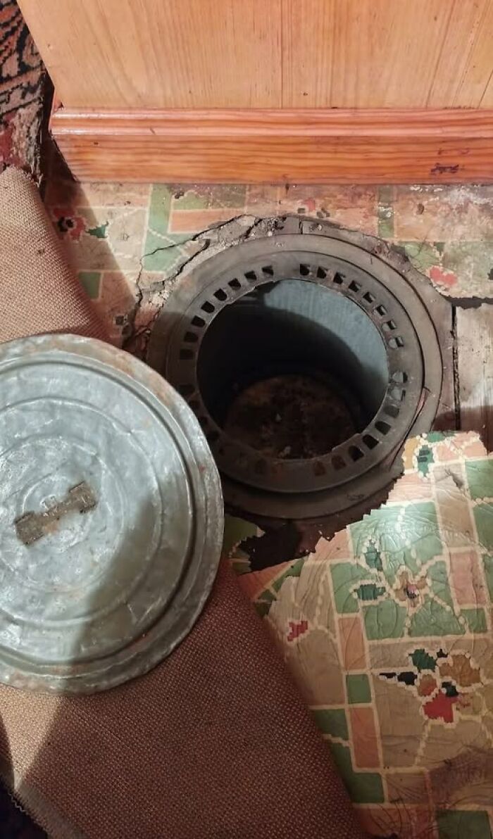 Old metal vent or hidden trapdoor uncovered beneath worn vintage flooring in a home with a forgotten or haunted past.