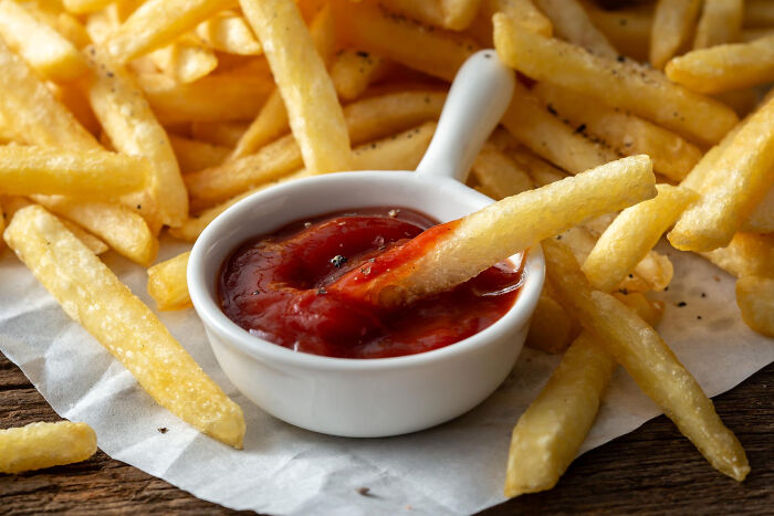 Crispy French fries seasoned with pepper being dipped into a white bowl of ketchup, illustrating wild cooking opinions.