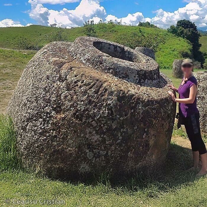 Large ancient stone jar in a grassy field with a person standing beside it, highlighting ancient history artifacts.