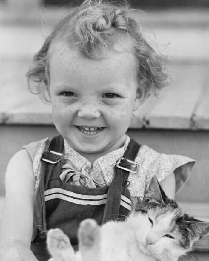 Smiling vintage photo of a child holding a relaxed cat, showcasing the timeless bond between kids and cats.