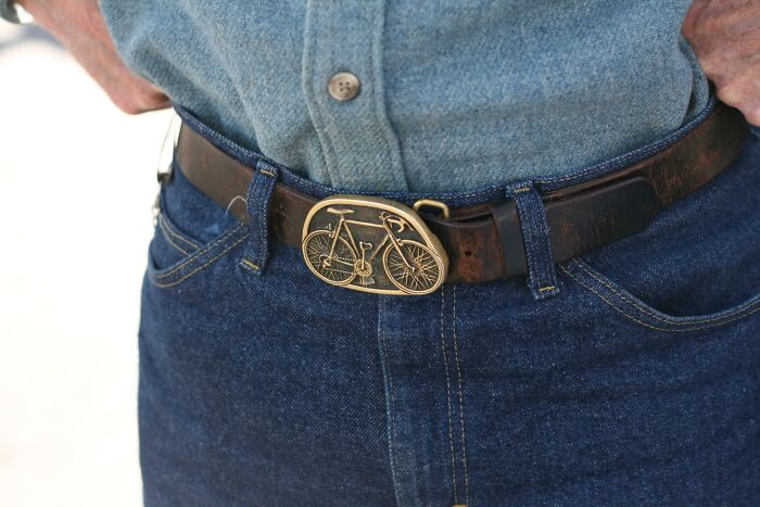 Close-up of a person wearing a blue denim shirt and jeans with a bicycle-themed belt buckle, an unusual find shared by doctors.