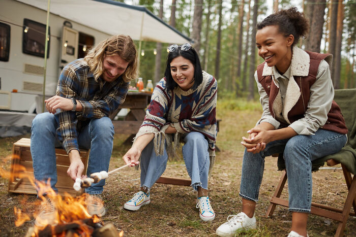 Three adults enjoying roasting marshmallows by a campfire, capturing moments like being picked last in gym class again.